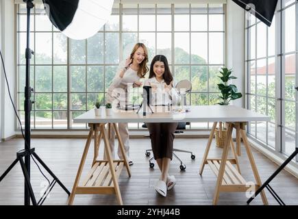 Zwei asiatische Frauen, die Inhalte für soziale Medien erstellen. Sie verwenden ein Studio-Setup, das ein Smartphone auf einem Stativ, Beleuchtungsgeräte und umfasst Stockfoto