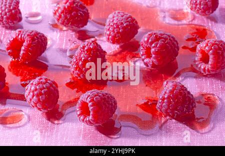 Himbeeren in Himbeersirup liegen auf einem rosafarbenen Glastisch. Stockfoto
