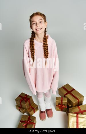 Ein entzücktes junges Mädchen, das einen rosa Pullover trägt, steht mit festlichen Geschenken und fängt Feiertagsstimmung ein. Stockfoto