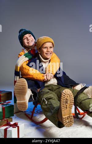 Zwei Jungs in gemütlicher Winterkleidung lächeln beim Schlitten in festlicher Atmosphäre. Stockfoto
