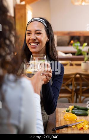 Mit Getränken toasten, Freunde lächeln in der gemütlichen Küche für Thanksgiving-Vorbereitungen, zu Hause Stockfoto