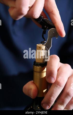 Rotwein wird mit einem Sommeliermesser entkorkt. Nahaufnahme der Hände, Kork, Flaschenhals. Wein wird mit einem Sommelier-Messer geöffnet. Stockfoto