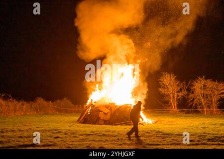 Ein großes Lagerfeuer, das auf einem Feld brennt, vor dem ein Mann läuft Stockfoto