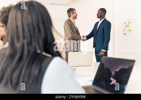 Verschiedene Geschäftsleute schütteln während einer Besprechung mit Teammitgliedern die Hand, die in einer modernen Büroumgebung beobachten Stockfoto