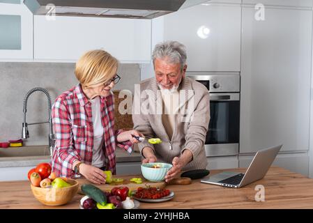 Seniorenpaar Mann und Frau kochen zusammen in der Hausküche zu Hause mit Laptop-Computer für neue Rezepte, die sie online im Internet finden. Spaß A Stockfoto