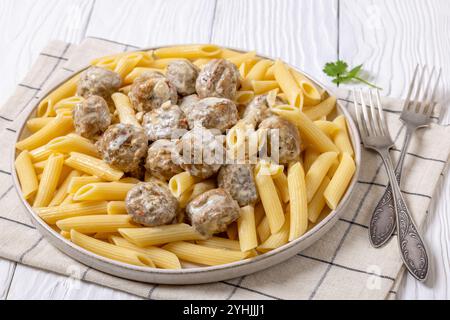 Gemahlene putenfleischbällchen mit Penne Nudeln auf Teller auf weißem Holztisch mit rustikalen Gabeln, horizontale Ansicht von oben, Nahaufnahme Stockfoto