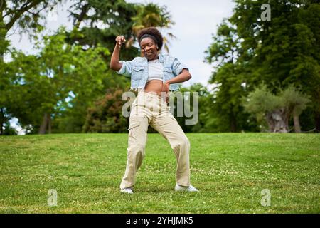 Eine Afrikanerin mit lockigem Haar, die eine Jeansjacke trägt, tanzt und genießt sich und strahlt Freude und Energie in ihren Bewegungen aus. Stockfoto