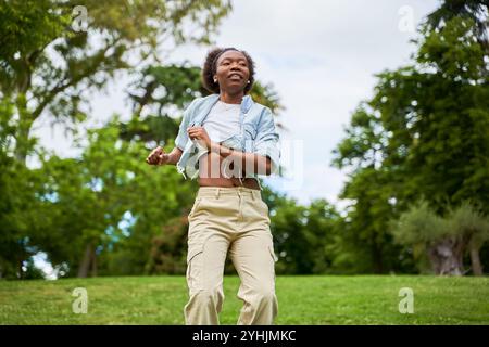 Eine Afrikanerin mit lockigem Haar, die eine Jeansjacke trägt, tanzt und genießt sich und strahlt Freude und Energie in ihren Bewegungen aus. Stockfoto