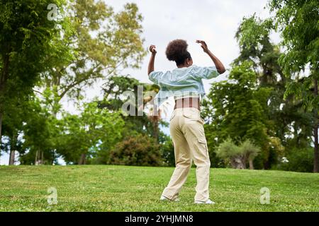 Eine Afrikanerin mit lockigem Haar, die eine Jeansjacke trägt, tanzt und genießt sich und strahlt Freude und Energie in ihren Bewegungen aus. Stockfoto