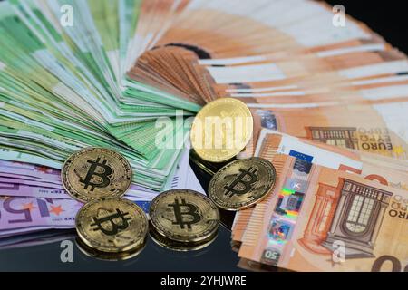 Goldene Bitcoin-Münzen sind neben einem Stapel Euro-Banknoten angeordnet und symbolisieren das Zusammenspiel zwischen traditioneller und digitaler Währung im modernen Finanzsektor Stockfoto