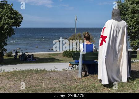 Ein Ritter mit rotem Kreuz auf weißem Mantel und Rüstung steht hinter einer Frau auf einer Bank mit Blick auf die Ostsee, Darsteller, Teilnehmer Stockfoto