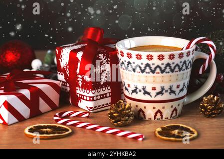 Kaffeetasse mit Weihnachtsmotiv und weihnachtsgeschenkboxen, weihnachtsbonbons und weihnachtsbeleuchtung auf einem Holztisch. Hintergrund des Weihnachtskonzepts Stockfoto