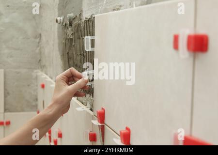 Frau, die die Wände des Badezimmers gefliest hat Flachwand-Nivelliersystem für Kunststofffliesen. Prozess der Installation von Fliesen im Badezimmer. Heimwerkerarbeit. Stockfoto