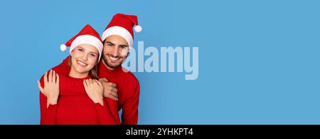 Fröhliches Paar Mit Roten Pullis Und Weihnachtsmänteln, Das Auf Blauem Hintergrund Posiert Stockfoto