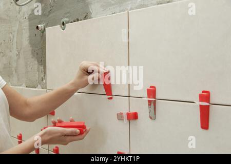 Frau, die die Wände des Badezimmers gefliest hat Flachwand-Nivelliersystem für Kunststofffliesen. Prozess der Installation von Fliesen im Badezimmer. Heimwerkerarbeit. Stockfoto