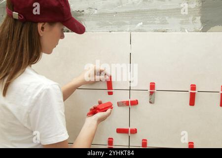 Frau, die die Wände des Badezimmers gefliest hat Flachwand-Nivelliersystem für Kunststofffliesen. Prozess der Installation von Fliesen im Badezimmer. Heimwerkerarbeit. Stockfoto