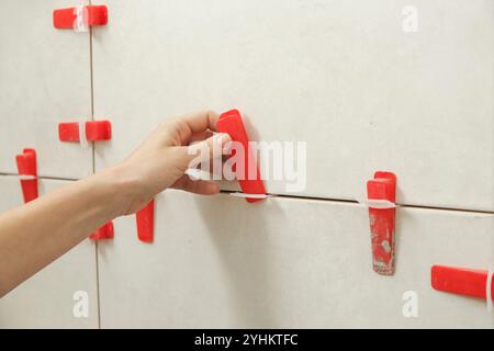 Frau, die die Wände des Badezimmers gefliest hat Flachwand-Nivelliersystem für Kunststofffliesen. Prozess der Installation von Fliesen im Badezimmer. Heimwerkerarbeit. Stockfoto