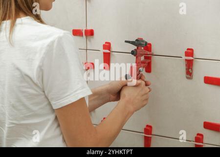 Frau, die die Wände des Badezimmers gefliest hat Flachwand-Nivelliersystem für Kunststofffliesen. Prozess der Installation von Fliesen im Badezimmer. Heimwerkerarbeit. Stockfoto