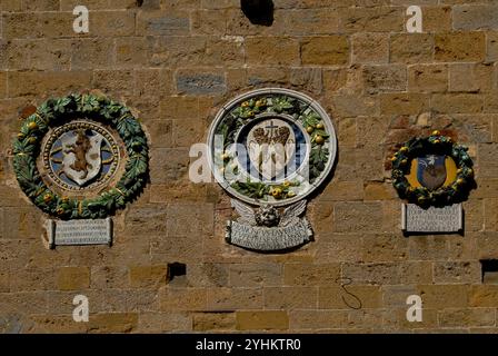 Wappen florentinischer Kommissare des späten 15. Jahrhunderts in Volterra, Toskana, Italien. Diese Medaillons oder Tafeln, die an der Fassade eines mittelalterlichen Palastes, dem Palazzo dei priori, ausgestellt sind, erinnern an die Herrschaft von Florenz und den Medici nach der Eroberung von Volterra durch Florenz im Jahr 1472. Der Palazzo dei priori, auch bekannt als Palazzo del Popolo (Volkspalast) und Municipio (Rathaus), ist der älteste Sitz der ständigen lokalen Verwaltung der Toskana und heute das Rathaus von Volterra. Stockfoto