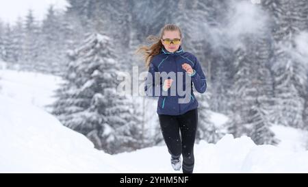 Teenager-Mädchen, das im Winter durch eine schneebedeckte Landschaft mit Bäumen herumläuft Stockfoto