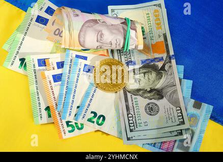 Bitcoin, Dollar, Euro und Hrywna auf dem Hintergrund der ukrainischen Flagge. Hilfe für das ukrainische Volk aus der Europäischen Union und den Vereinigten Staaten Stockfoto