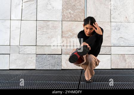 Eine junge Frau in braunen Hosen und schwarzem T-Shirt Breakdance, die auf einem Metallgitter posiert. Sportlichkeit und Geschicklichkeit, wie es die Frau kann Stockfoto