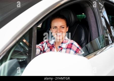 Portrait einer weißen Frau, die ein weißes Auto fährt und lächelt. Stockfoto