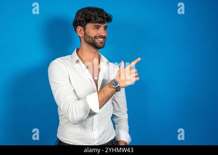 Junger Geschäftsmann, der mit dem Finger zeigt, was Interessantes auf blauem Hintergrund zeigt Stockfoto