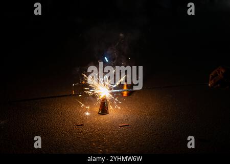 Eine Hand zündet einen bunten Diwali-Springbrunnen an, der Funken vor dunklem Hintergrund duscht. Festliche Feier und Licht in der Nacht. Stockfoto