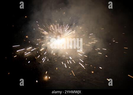 Helle Funken brechen aus einem Feuerwerk auf dem Boden auf und strahlen Licht und Rauch vor einer dunklen Kulisse aus. Stockfoto