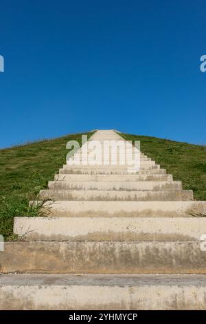 Eine lange Treppe führt auf einen Green Hill unter dem blauen Himmel. Betontreppen führen an einem sonnigen Tag auf einen grasbewachsenen Hügel. Vertikales Foto. Niemand, Kopierraum für Stockfoto