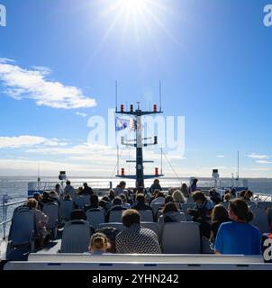 Ein überfülltes Deck eines Schiffes unter der hellen Sonne, mit den Passagieren genießen Sie den malerischen Blick auf das Wasser und den Himmel. Stockfoto