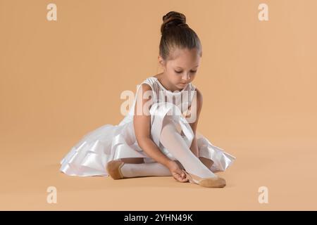 Kleine Ballerina, die spitzenschuhe vor beigefarbenem Hintergrund anzieht Stockfoto