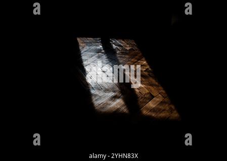 Schwarzer Schatten, der vom Licht projiziert wird, das aus einem Fenster hereinkommt und nur den alten Holzboden beleuchtet Stockfoto