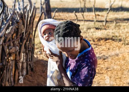 afrikanische Dorfbewohner, ein junges Mädchen, das ein Baby hält, ungewollte Teenager-Schwangerschaft, geflochtene Haare Stockfoto