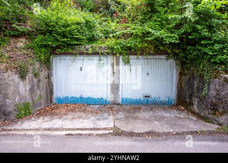 Zwei Garagentore weiß und blau mit Efeu und Grün über verlassenen und verwitterten Türen mit blau-weiß-verblassen Stockfoto