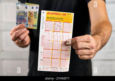 Bayern, Deutschland - 12. November 2024: Lotto 6 von 49 Zahlen Lottoticket oder Lottospielzettel aus der Staatslotterie. Symbol, der Gewinner hält das Glücksspiel in der Hand, neben Banknoten und Eurogewinnen des Glücksspiels. *** Lotto 6 aus 49 Zahlen Lotto-Tippschein, bzw. Lotto-Spielschein der staatlichen Lotterie. Symbol, Gewinner hält Glückslos in der Hand, neben Geldscheinen und Euro-Gewinn des Glücksspieles. Stockfoto