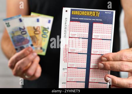 Bayern, Deutschland - 12. November 2024: EuroJackpot-Ticket oder Lotterie-Ticket. Symbol, der Gewinner hält das Glücksspiel in der Hand, neben Banknoten und Eurogewinnen des Glücksspiels. *** Eurojackpot Tippschein, bzw. Spielschein der Lotterie. Symbol, Gewinner hält Glückslos in der Hand, neben Geldscheinen und Euro-Gewinn des Glücksspieles. Stockfoto