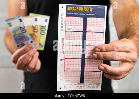 Bayern, Deutschland - 12. November 2024: Symbolisches Bild für Eurojackpot. Der Gewinner hält das Eurojackpot-Ticket neben dem Gewinngeld oder den Euro-Banknoten der Lotterie in der Hand. *** Symbolbild zu Eurojackpot. Gewinner hält Eurojackpot-Schein, bzw. Spielschein in der Hand neben Geld-gewinn, bzw. Euro-Banknoten der Zahlenlotterie. Stockfoto