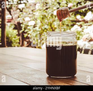 Glasgefäß mit Honig und Holzspender auf einem Tisch mit unscharfem Hintergrund. Stockfoto