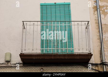 Alte Hausfassade mit rostigem Balkon und grünem Jalousien in Spanien. Stockfoto