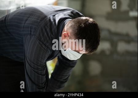 Ein Mann in einer Maske auf dem Hintergrund einer Wand aus Blöcken führt Reparaturarbeiten durch, eine minimale Schutzmaske gegen Schießpulver. Stockfoto