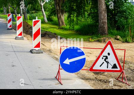 Ein Straßenreparaturbereich, der durch Warn- und Richtungsschilder sowie rot-weiß gestreifte Pfosten und Warnschilder abgegrenzt ist Stockfoto