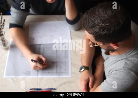 Ein Blick von oben auf die Hände von Architekten, die an detaillierten Bauplänen arbeiten. Szene nimmt Skizzen und Blaupausen auf einem Schreibtisch mit Händen auf Stockfoto