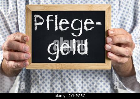 Bayern, Deutschland - 12. November 2024: Pflegegeld, älterer Patient im Patientenkleid mit Schild. Symbolisches Bild für Barzahlungen und Leistungen in der Pflege oder in Pflegeberufen. *** Pflegegeld, älterer Patient im Patientenkittel mit Schild. Symbolbild für Geld-Zahlungen und Leistungen in der Pflege, bzw. In Pflegeberufen. Stockfoto