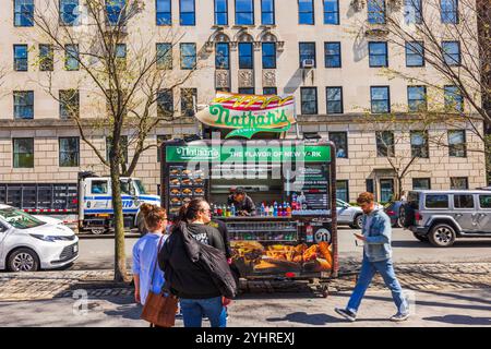 Nathans berühmter Hotdog-Stand in New York City, an dem die Leute am sonnigen Frühlingstag vorbeifahren, gegen ein NYPD-Fahrzeug im Hintergrund. New York. USA. Stockfoto