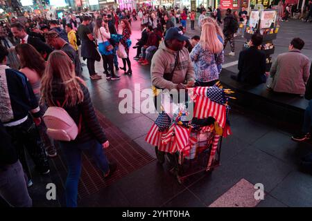 New York, New York, USA. November 2024. Ein Mann verkauft amerikanische Flaggen und Kamala Harris Waren aus einem Wagen am Times Square am Wahltag, nur wenige Stunden bevor die Wahllokale schließen und die Ergebnisse eintreffen. (Kreditbild: © Edna Leshowitz/ZUMA Press Wire) NUR REDAKTIONELLE VERWENDUNG! Nicht für kommerzielle ZWECKE! Stockfoto