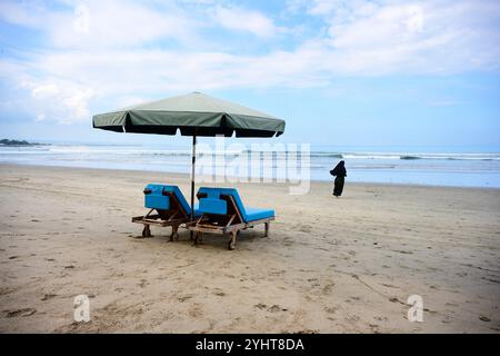 Kuta Beach auf Bali mit Sonnenschirm, Strandliege und einer laufenden muslimischen Frau, die einen Hijab trägt Stockfoto