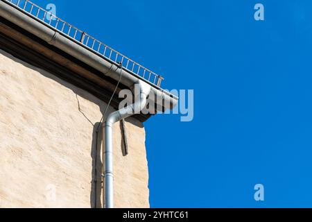 Hellblauer Himmel über dem Dach eines alten Gebäudes mit einer grauen Metallrinne für Regenwasser und einer weißen Pfeife an einem sonnigen Tag. Konzept für Kopierbereich. Stockfoto