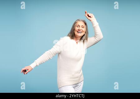 Porträt einer glücklichen, lächelnden Seniorin mit geschlossenen Augen, tanzend, lustig, isoliert auf blauem Hintergrund. Hobby-Konzept Stockfoto